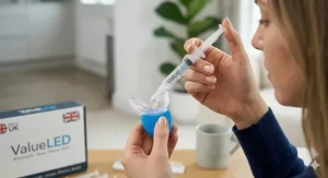 A close-up of a woman precisely applying whitening gel from a ValueLED syringe into a clear mouth tray for a home treatment.