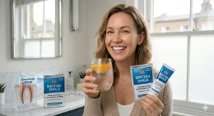 A British woman smiling while holding a glass of iced water and a pack of whitening strips formulated specifically for sensitive teeth.
