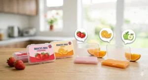 Illustration of strawberry and orange flavoured wax for children's braces, featuring detailed fruit icons and UK-style product labelling in a naturally lit kitchen.