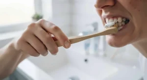 Side profile of a person brushing their teeth with a soft-bristled toothbrush using gentle circular motions along the gum line.