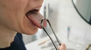Step-by-step diagram showing the correct technique for placing and pulling a tongue scraper from back to front to clear plaque.